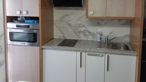 Une cuisine compacte dotée de meubles en bois, d’un four encastré, d’un micro-ondes, d’un évier et d’un petit coin repas avec deux chaises.