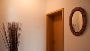 Un pasillo con una puerta de madera, un espejo en la pared y una planta decorativa alta.