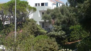 Un edificio blanco de dos pisos con techo de tejas rojas, rodeado de abundante vegetación y árboles.
