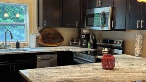 Cocina con armarios oscuros, encimera de granito, microondas, cafetera y un letrero de madera que dice 'Welcome to the Lake'.