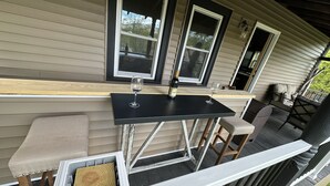 Un espacio al aire libre cubierto con una mesa negra y dos sillas, una botella de vino y una copa sobre la mesa.