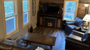 Una sala de estar acogedora con chimenea, sofás de cuero, una mesa de centro de madera y un reloj grande en la pared.