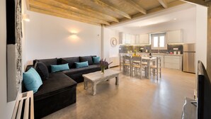 Een moderne woonkamer met een donkere bank, teal kussens, een houten salontafel en een eethoek met een witte tafel en stoelen.