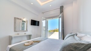 Een moderne slaapkamer met een bed, nachtkastje, flatscreen televisie en een groot raam met uitzicht op de natuur.