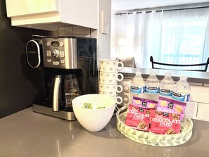 A kitchen with a coffee maker, a bowl, and a tray with water bottles and chocolate chip cookies.