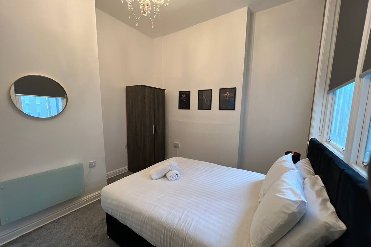Une chambre à coucher avec un lit, une armoire, un lustre, un miroir et des tableaux encadrés accrochés au mur.