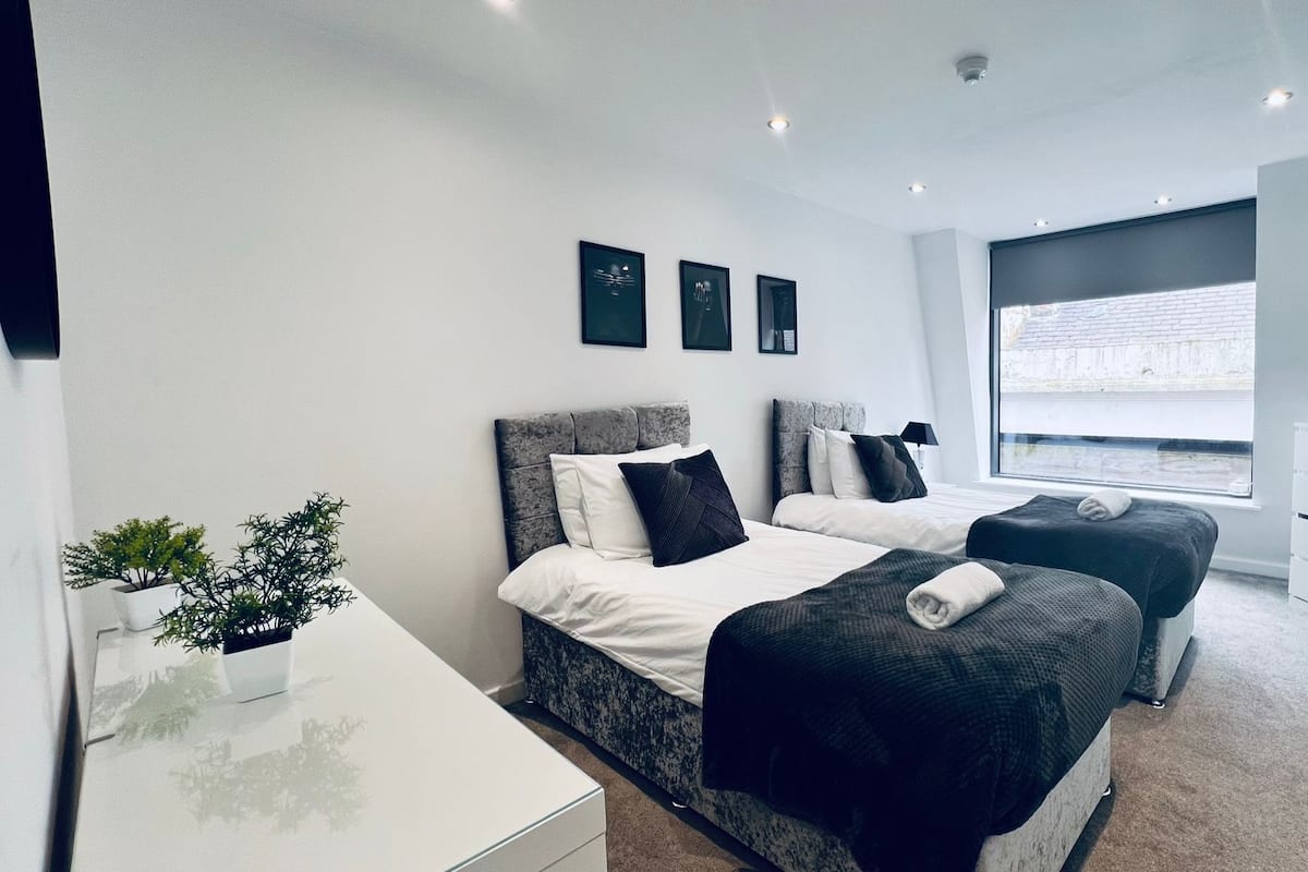 Une chambre moderne avec deux lits, une commode blanche, un petit bureau et une fenêtre donnant sur un beau paysage.