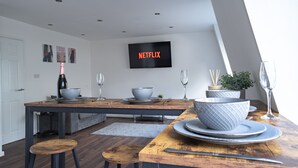 A modern kitchen with a wooden dining table, white bowls, and a TV displaying 'NETFLIX'. - Designer Apartments (Liverpool)