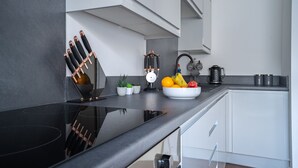 A modern kitchen with a black countertop, white cabinets, a bowl of fruit, and a wine rack. - Designer Apartments (Liverpool)