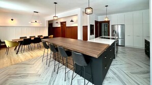 Een moderne keuken met een groot kookeiland, hanglampen en een eethoek met stoelen.
