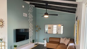 A modern living room with a brown leather sofa, a wooden chair, a TV mounted on the wall, a floor lamp, and a ceiling fan. - Desert Oasis near Downtown Las Vegas (Las Vegas)