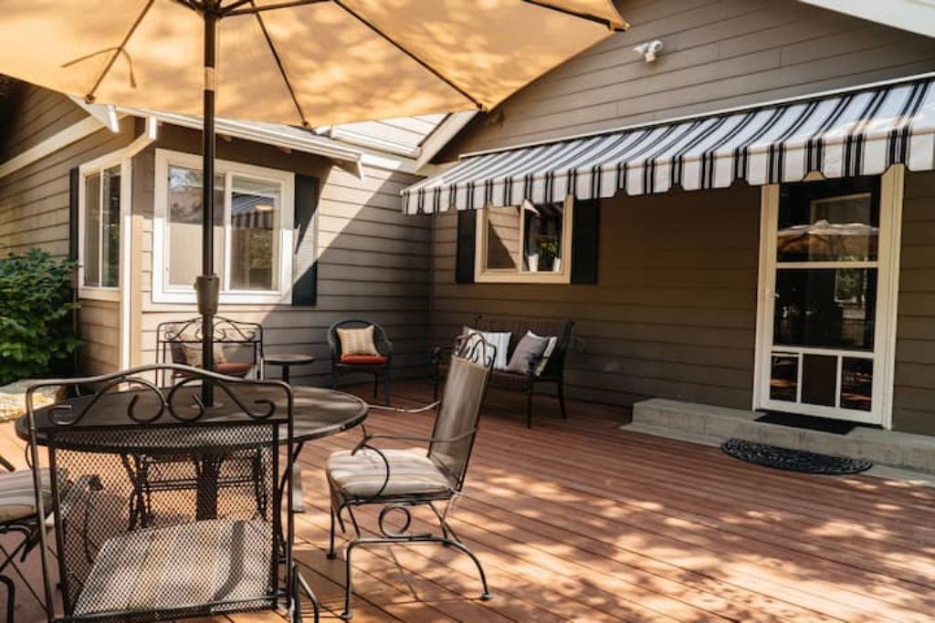 A patio with a table and chairs, a large umbrella, and a striped awning.