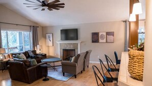 Amplia sala de estar con chimenea, un televisor montado encima y un comedor con sillas y una mesa.
