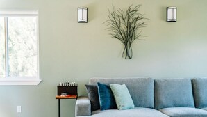 Una habitación con un sofá seccional gris, una mesita auxiliar pequeña y apliques de pared.