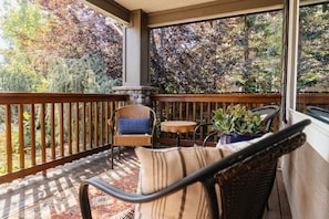 A covered porch with wicker furniture, a small table, and potted plants.