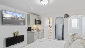 A modern hotel room with a bed, a flat-screen TV mounted on the wall, a kitchenette with a microwave, and a refrigerator. - The Knolls (Martinsburg)