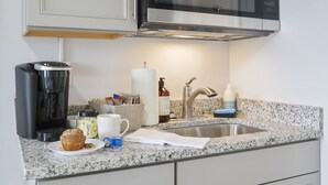A kitchen with white cabinets, a stainless steel microwave, a coffee maker, and a sink. - The Knolls (Martinsburg)