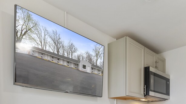 A modern kitchen with white cabinetry, a flat-screen TV mounted above the counter, and a small potted plant on the countertop. - The Knolls (Martinsburg)