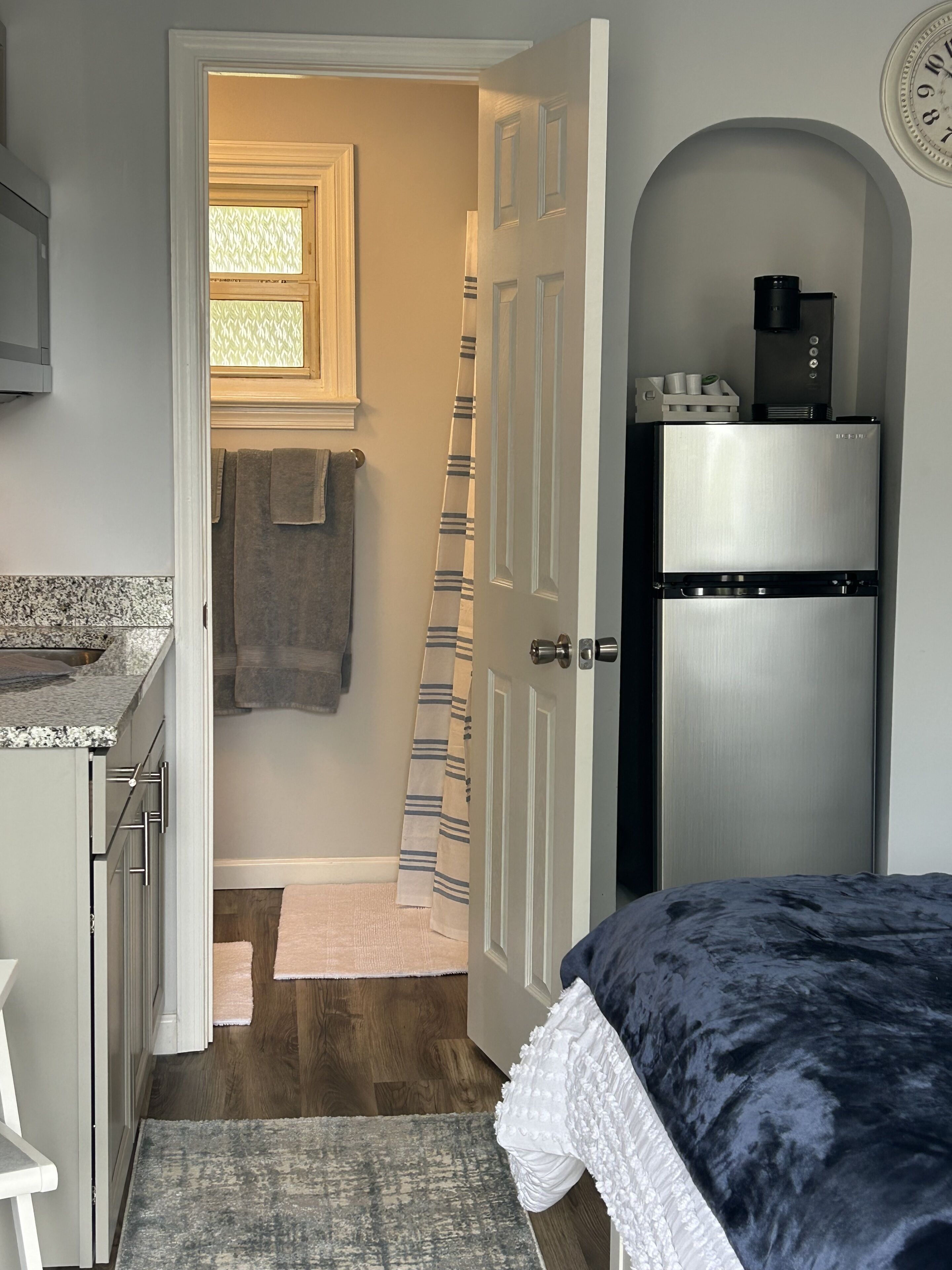 A compact kitchen with a refrigerator, a coffee maker, and a window with blinds.