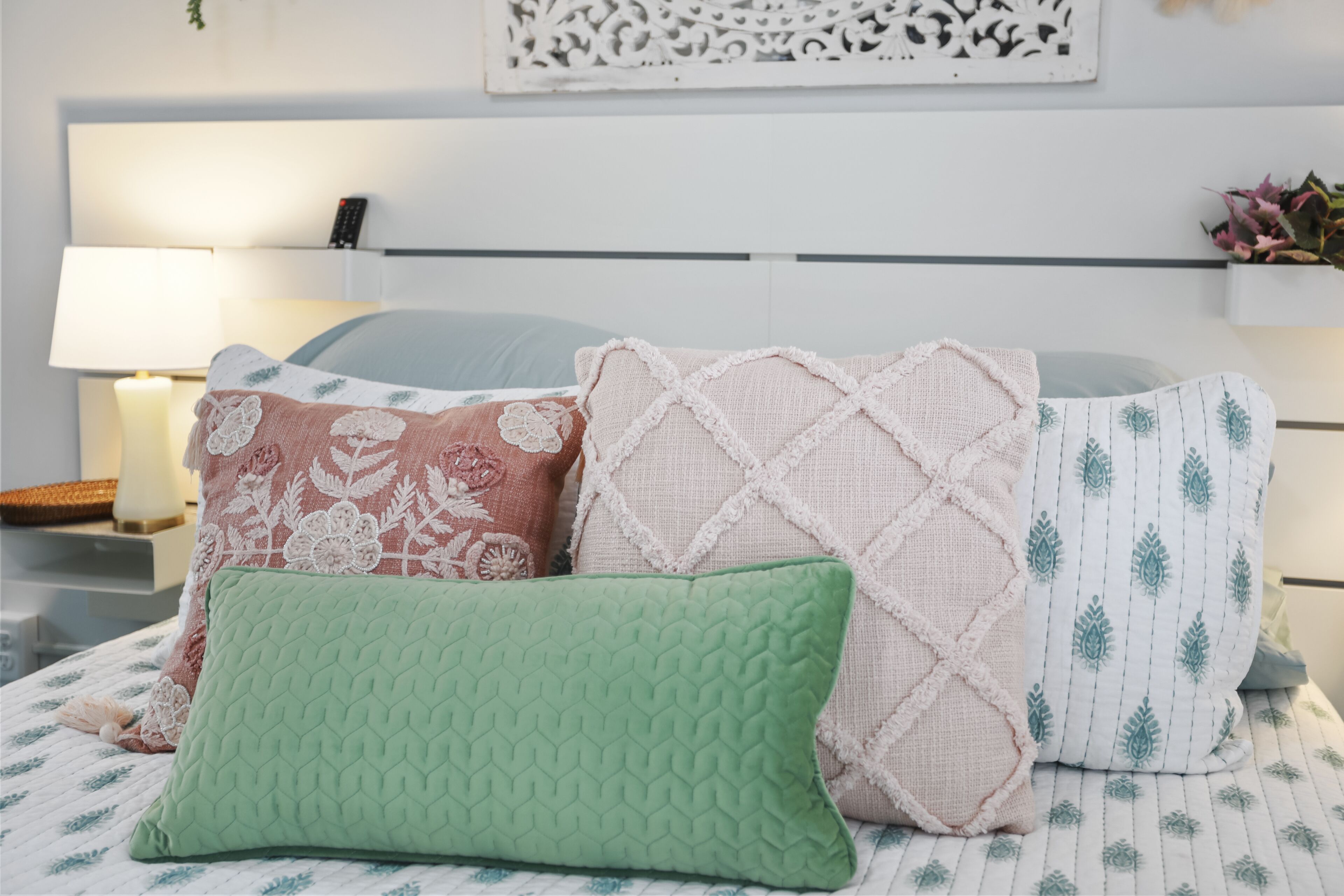 Una cama cuidadosamente ordenada con cuatro almohadas y una mesita de noche con lámpara y control remoto.