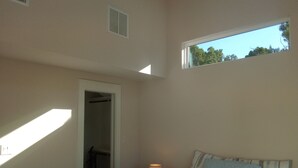 Una camera da letto con un letto, una finestra, una porta e una griglia di aerazione al soffitto.