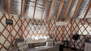 Um quarto aconchegante com um sofá cinzento, paredes de treliça de madeira, um ventilador e uma pequena mesa com um vaso.