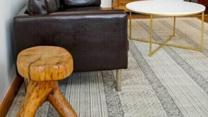 Ein Wohnzimmer mit einem dunkelbraunen Ledersofa, einem runden weißen Tisch, einem hölzernen Hocker und einem gemusterten Teppich.