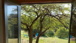 Eine Glastür öffnet sich zu einem Rasenstück mit Baum und blauem Stuhl.