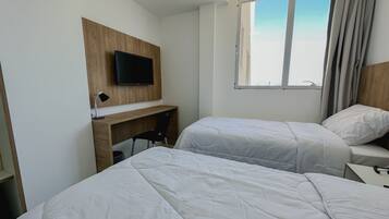 Quarto de hotel com duas camas, uma mesa, uma televisão e uma janela com cortinas.