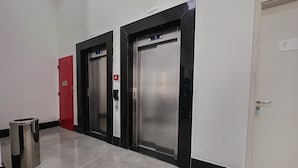 A hallway with two elevators, a red door, and a trash bin. - GO INN ARACRUZ (Aracruz)