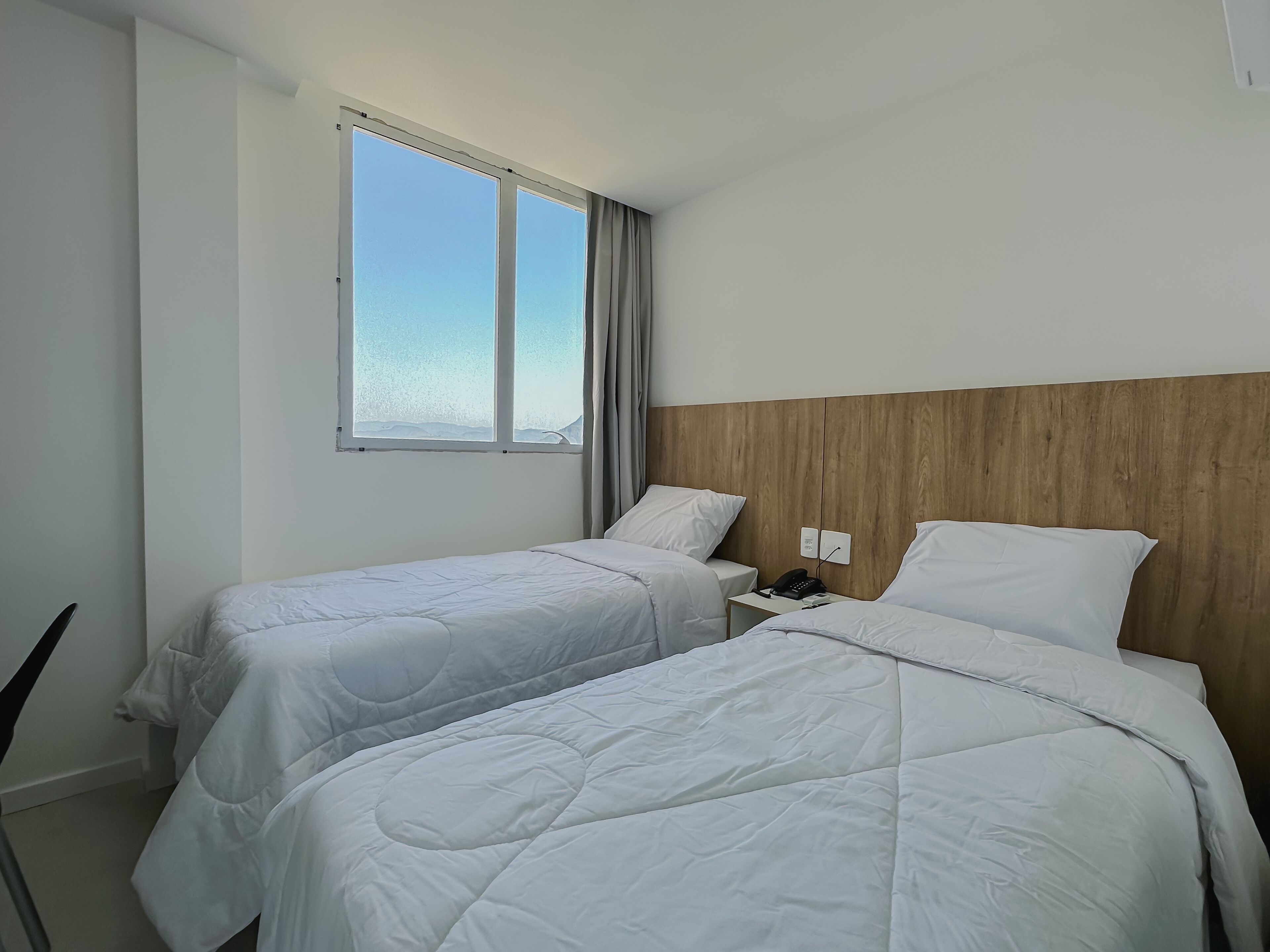 Habitación de hotel con dos camas individuales, cabecera de madera, mesita de noche con teléfono y ventana con vista al mar.