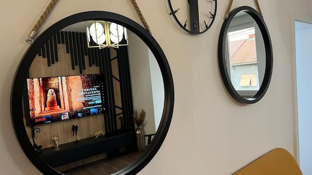 Huoneessa on suuri peili, kaksi seinäkelloa ja televisio, josta näkyy elokuvan kohtaus.