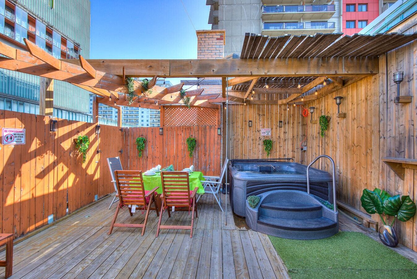 Una terraza de madera con un jacuzzi, una mesa con sillas y una cerca de madera.