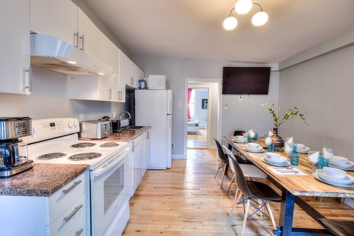Una cocina moderna con armarios blancos, una estufa y un comedor con una mesa y sillas de madera.