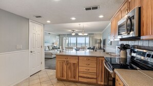 Une cuisine moderne avec des meubles en bois, un grand îlot central, des appareils électroménagers en acier inoxydable et une vue sur l’espace de vie.