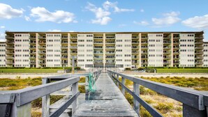 Une longue jetée en bois qui mène à un immeuble résidentiel de grande hauteur, doté de nombreux balcons.