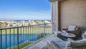A balcony with wicker furniture, a small table with a vase, and a view of the ocean and houses. - Ocean Park 318 Harbor Point - Hosted By Moore AI Rentals (Fernandina Beach)