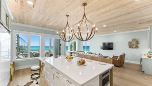 Une cuisine spacieuse dotée d’un grand îlot central, d’un plafond en bois et offrant une vue sur l’océan.
