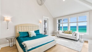 Une chambre avec un grand lit, un canapé blanc et une vue sur l’océan.