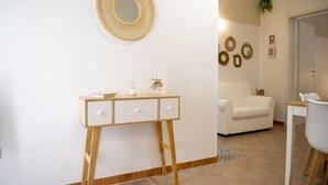 Un salón moderno con un sofá blanco, una consola de madera con cajones, un espejo redondo y adornos colgados en la pared.