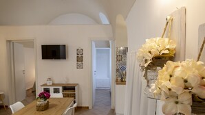 Un comedor con una mesa y sillas de madera, un televisor montado en la pared y un pasillo que conduce a un baño.