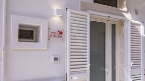 Un edificio blanco con una ventana y una puerta con contraventanas. Hay un letrero en la pared que dice "DIMORA Le Due Rose".