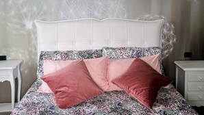 A bedroom with a white headboard, floral bedding, and pink pillows.
