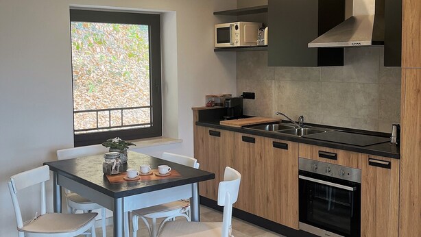 A modern kitchen with a dining area, featuring a built-in microwave, stainless steel range hood, and a large window with a view of greenery.