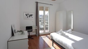 A bedroom with a bed, a desk, a chair, a world map, and a window with a view of buildings.