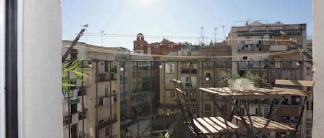 A balcony with a wooden table and chairs, a potted plant, and a view of a densely packed urban area with buildings.