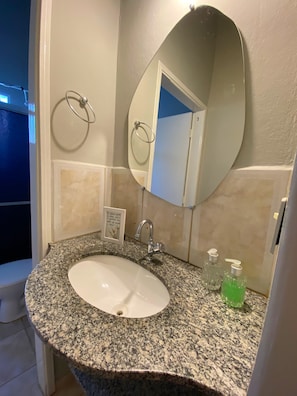 A bathroom with a granite countertop, a white sink, a mirror, and two soap dispensers. - Pousada Vila Tadeu (São João Batista do Glória)