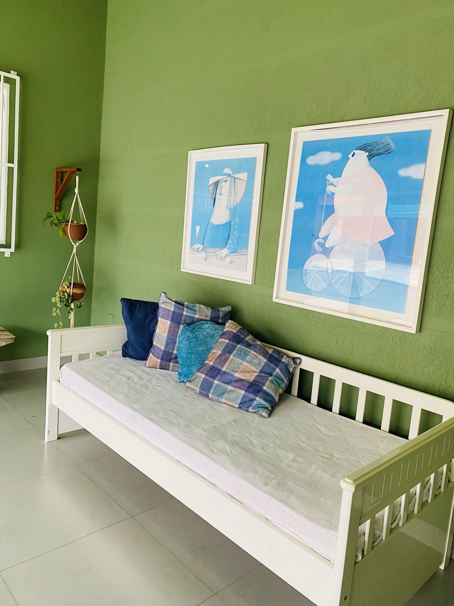 Ein weißes Bett mit kariertem Überwurf und Kissen, grüne Wände und zwei gerahmte Kunstwerke.