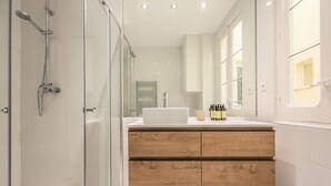 Une salle de bain moderne avec une douche à parois de verre, un meuble-lavabo en bois doté de tiroirs et un grand miroir.