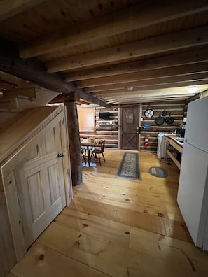 A wooden interior with a dining area, kitchen, and a large wooden door.